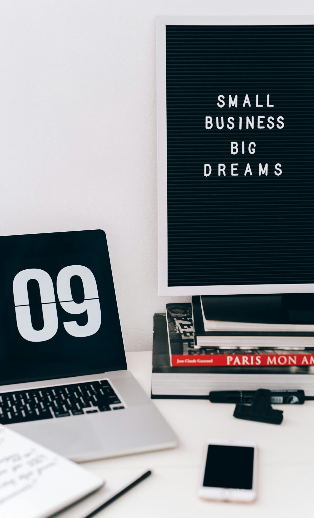 Modern workspace featuring a laptop, smartphone, and motivational quote board.